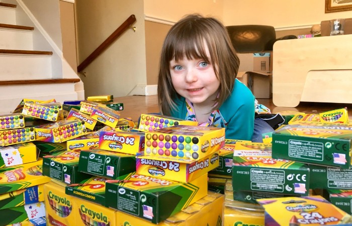 Smiling girl near a stack of crayons.