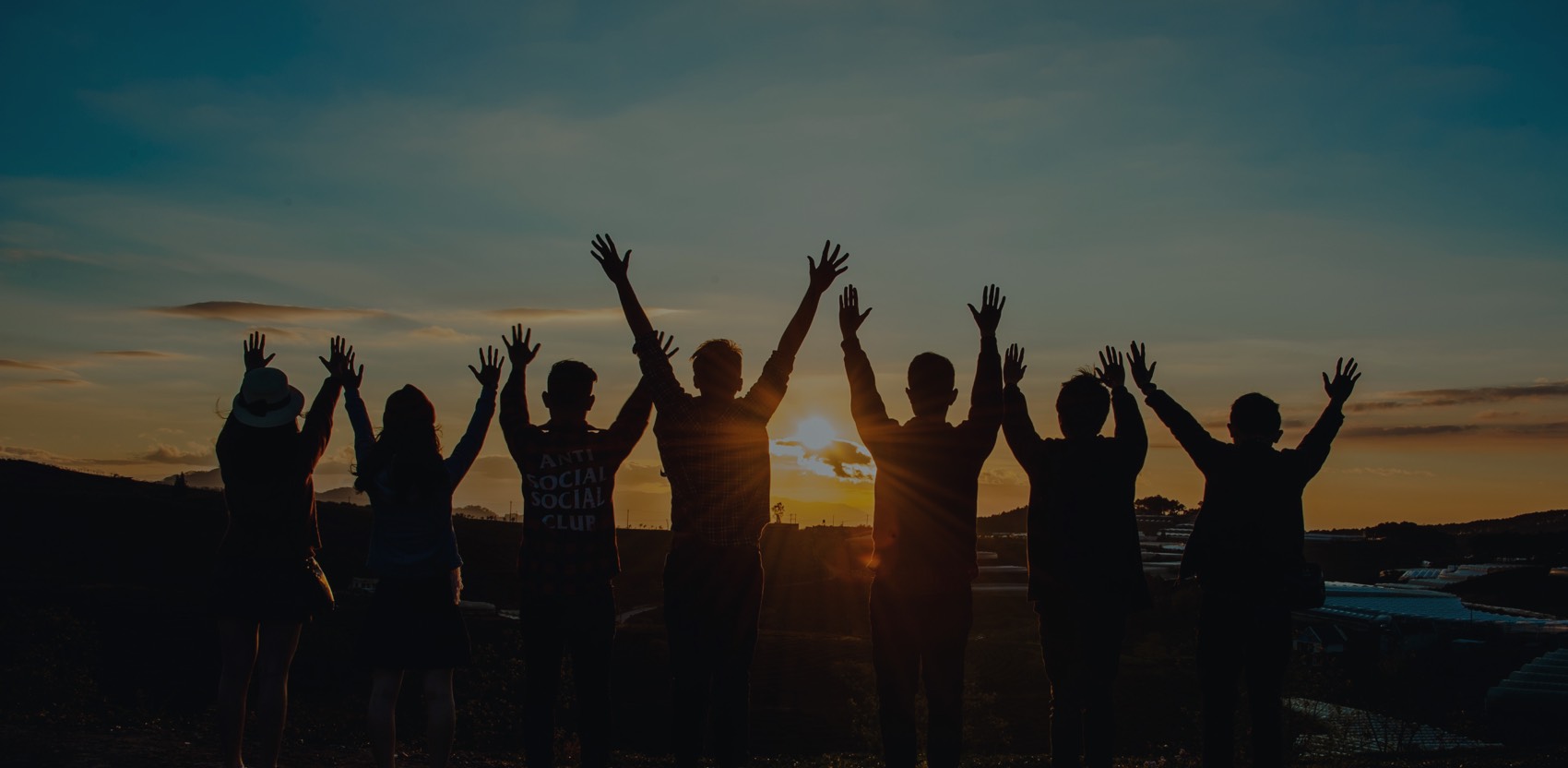 Group raising hands in front of sunset.