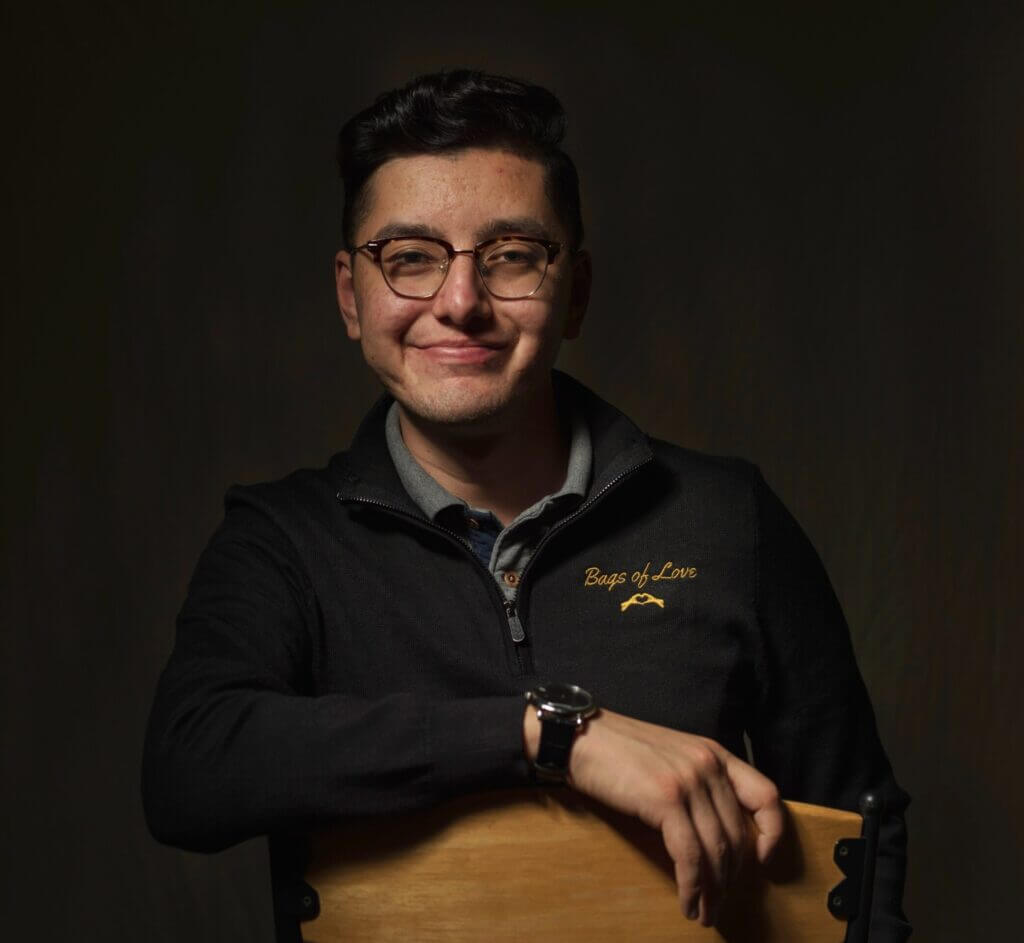 Julian Castaneda wearing glasses and a black sweater sitting on a chair.